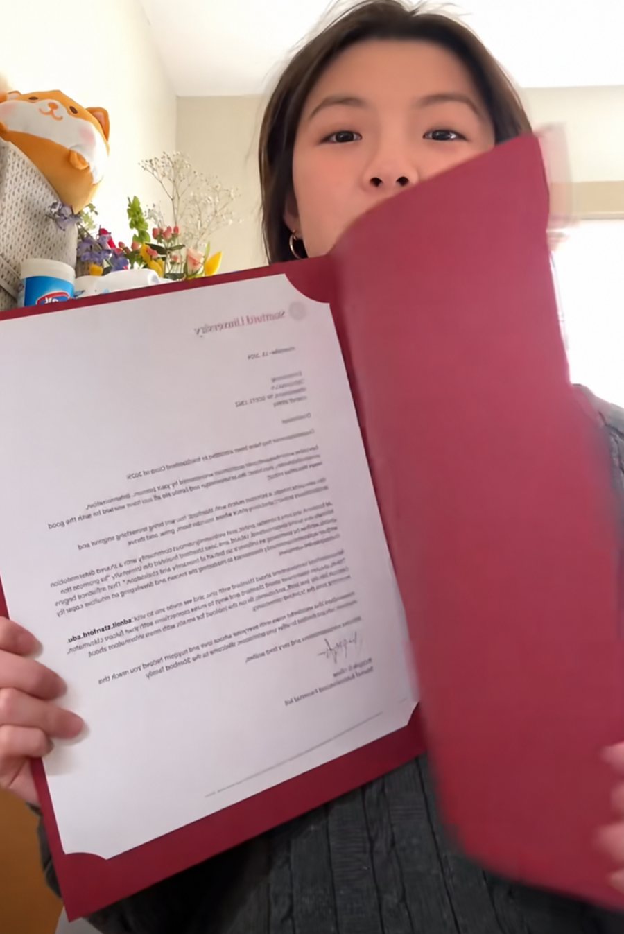Alaina Zhang holding her Stanford admission letter in the red Stanford folder